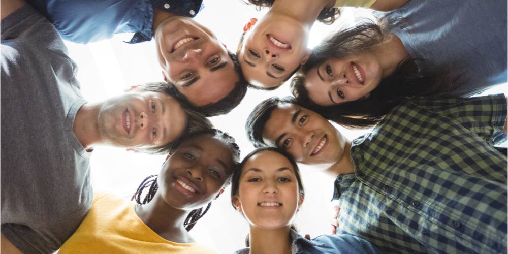 Fotografía de personas jóvenes sonrientes en círculo con las cabezas juntas sonriendo.