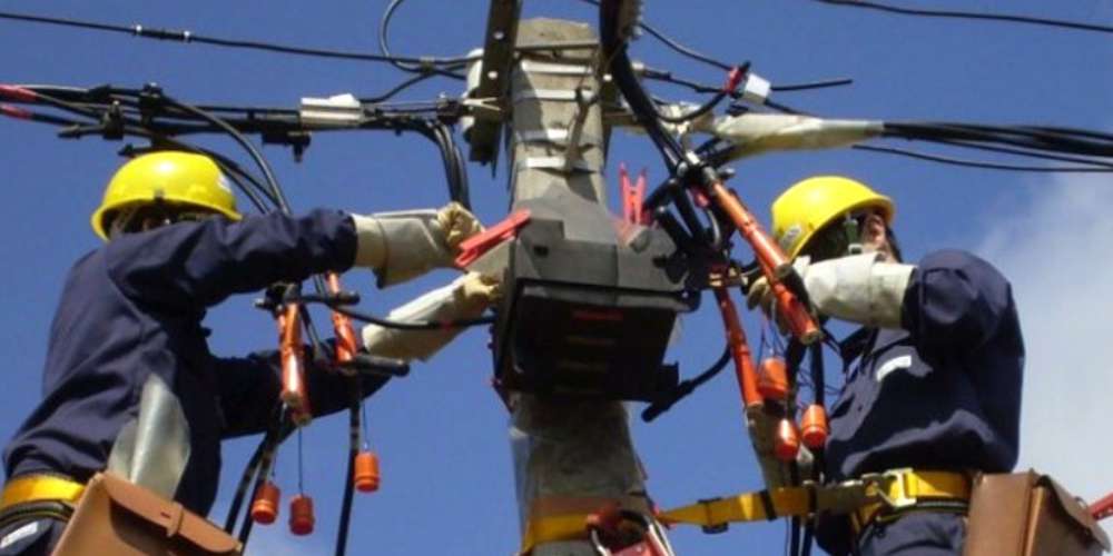 Fotografía de dos funcionarios de UTE trabajando en una columna del tendido eléctrico.