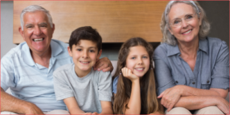 Fotografía de abuelos y nietos sonrientes, sentados en un sofá de living.