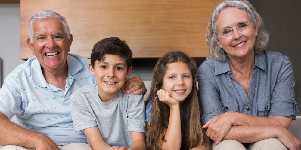 Fotografía de abuelos y nietos sonrientes, sentados en un sofá de living.